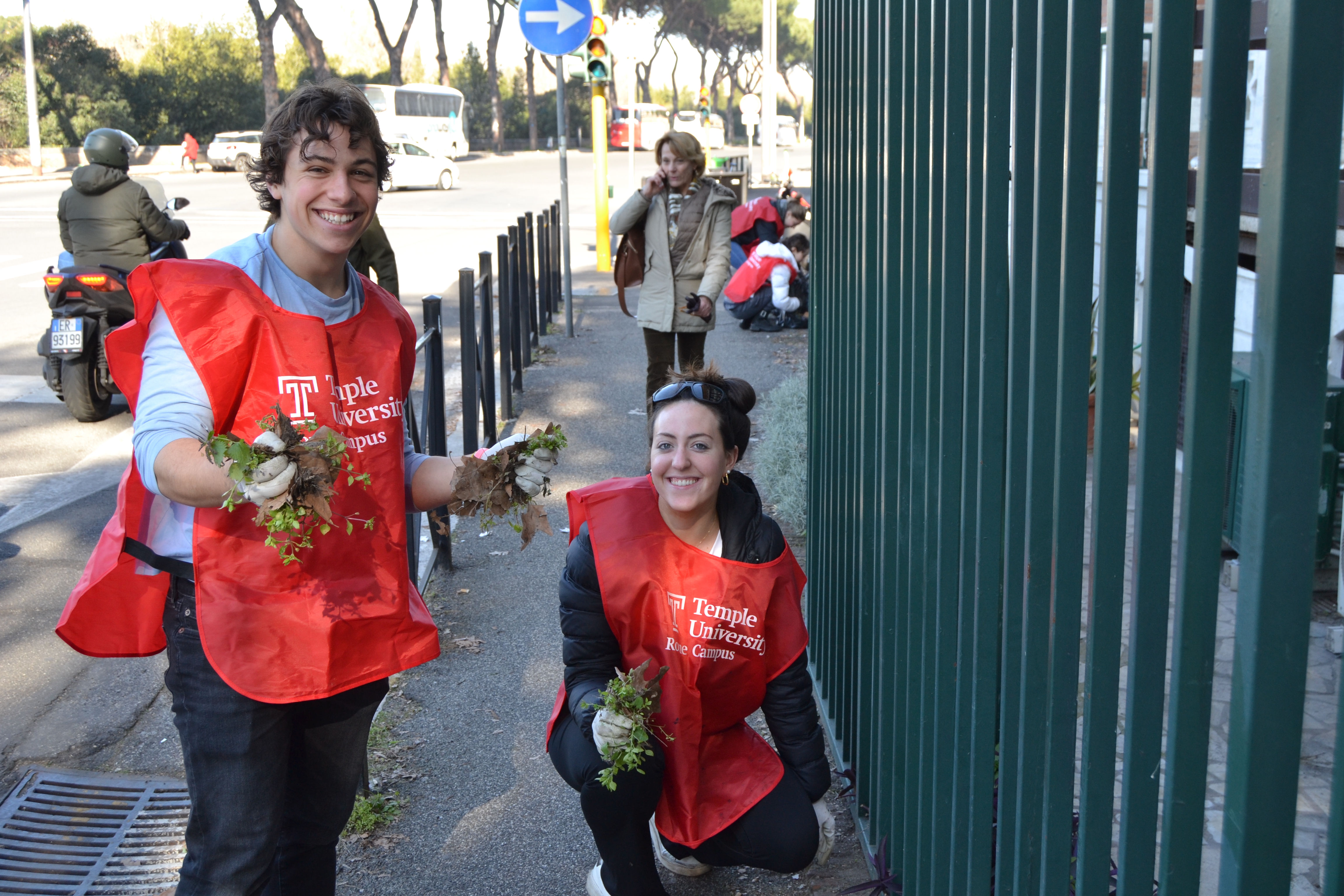 two students smiling while holding weeds they cleaned from the sidewalk