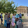 Group of people standing in circle and talking in front of Paestum monument