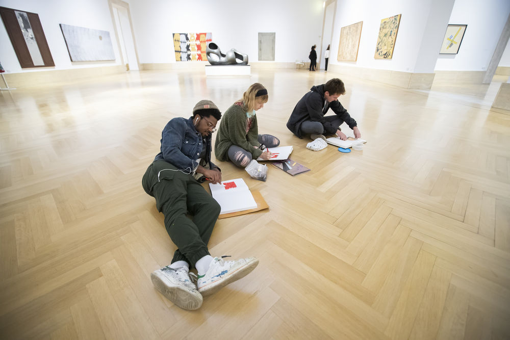 Three students sitting on floor of museum drawing in sketchbooks