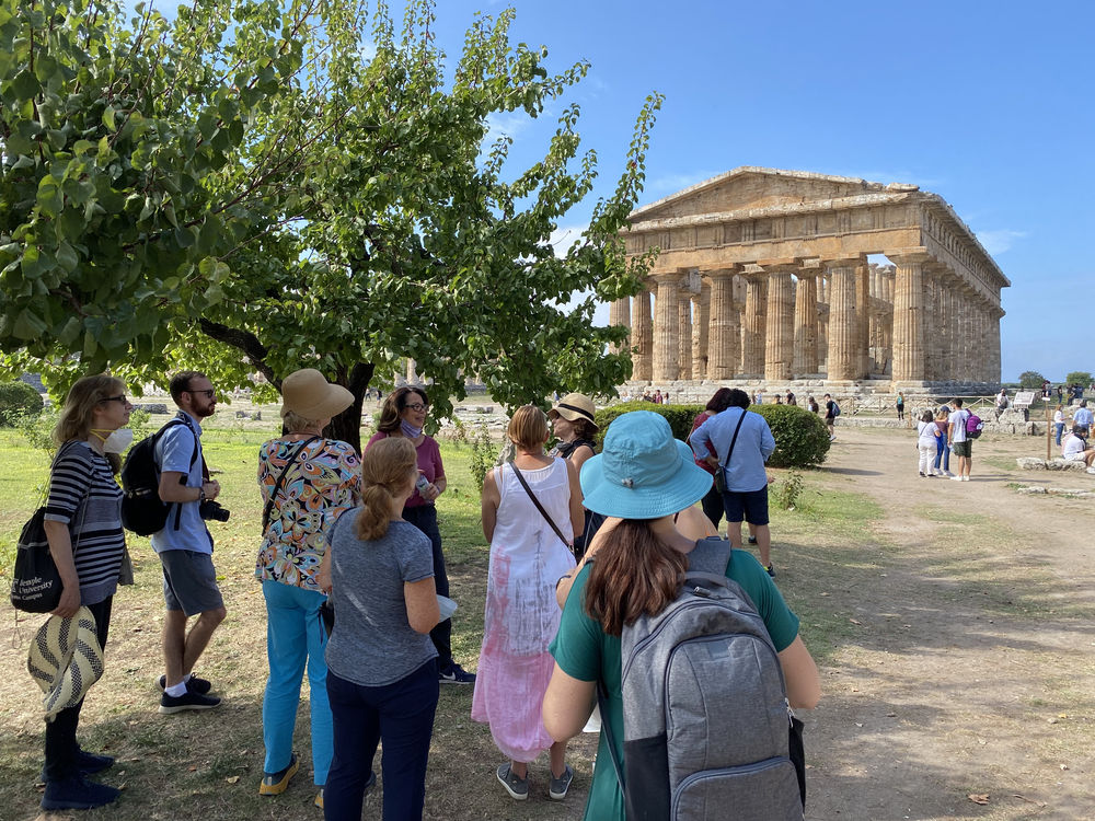 Group of people standing in circle and talking in front of Paestum monument