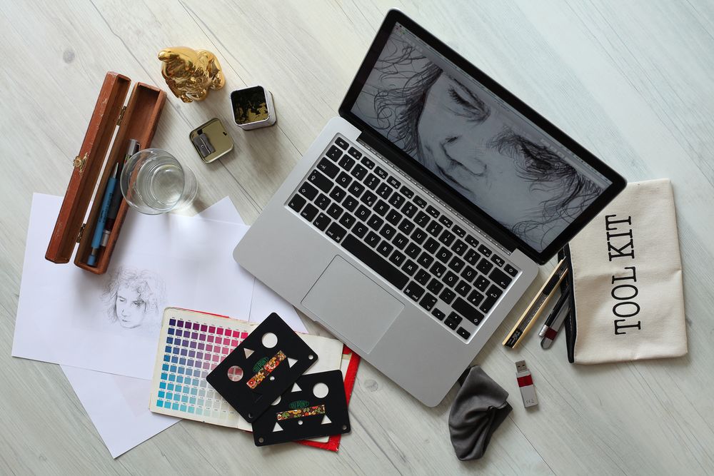 table with laptop and drawing materials, laptop has image of digital drawing of a portrait